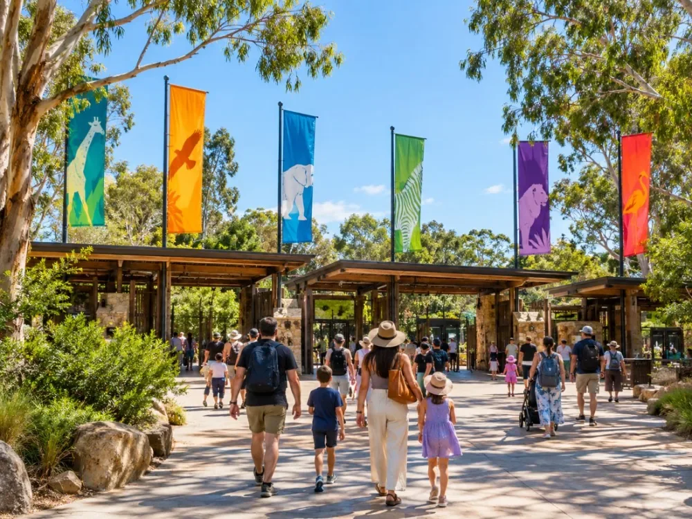 A zoo main entrance with tall flags and visitors walking in